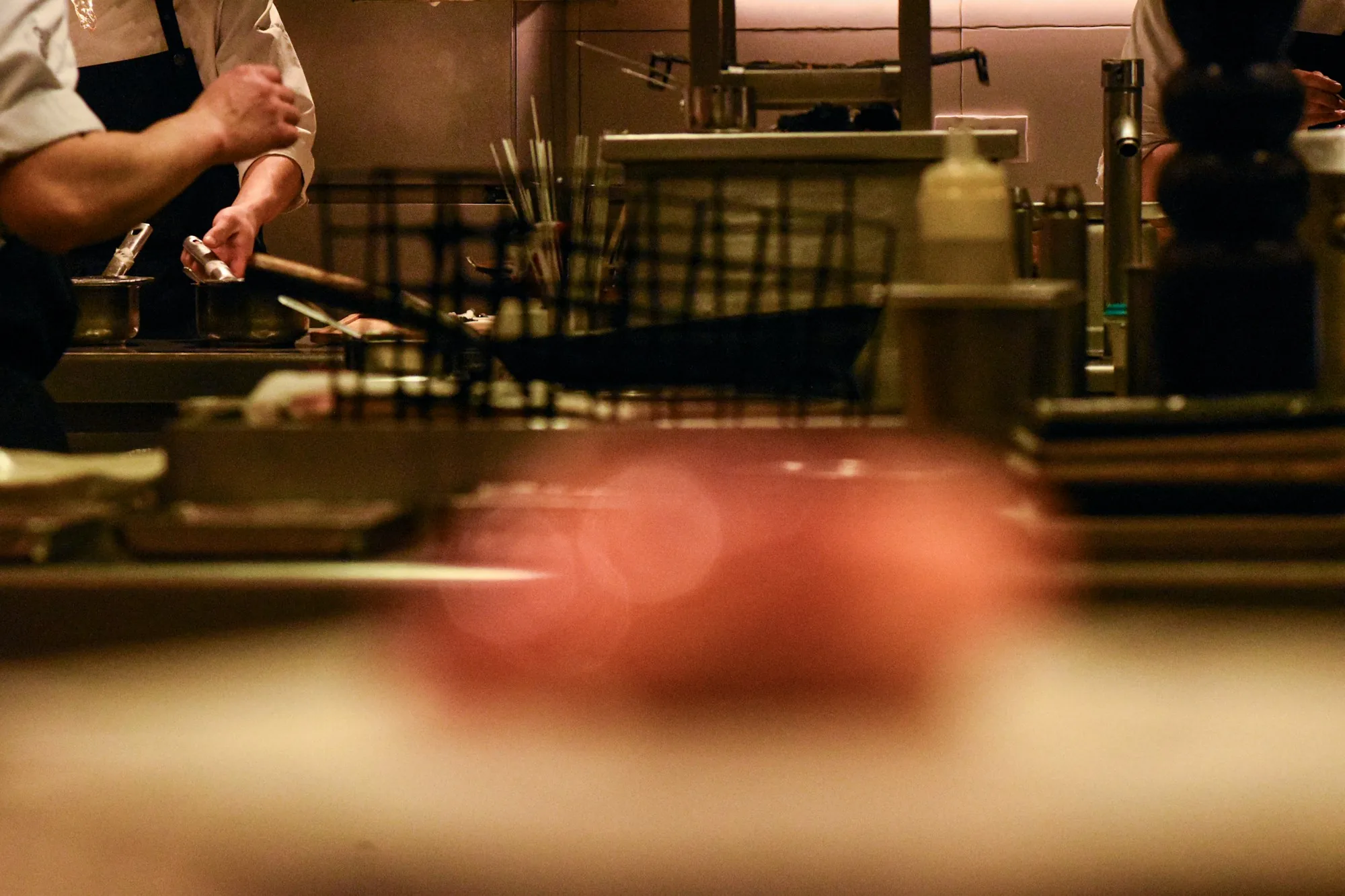 A chef's hands working a station in a warm-lit restaurant kitchen — the human labor that drives restaurant labor cost